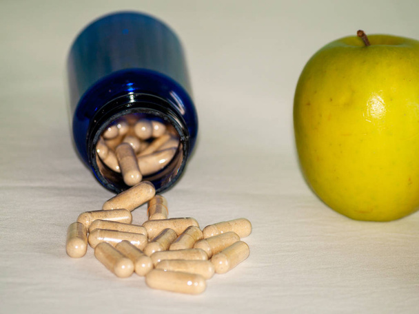 Яблоко и синий контейнер с таблетками растительного волокна на столе
 - Фото, изображение