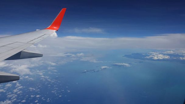 POV Mirando una hermosa isla exótica y el mar azul desde un avión comercial. Increíble vista del asiento de la ventana de pequeñas nubes hinchadas que proyectan una sombra sobre el océano y el continente desapareciendo en la distancia
 - Foto, imagen