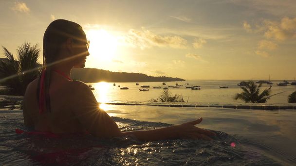Close Up, lencse fényfolt: Női utas a gondtalan nyaralás úgy néz ki, gyönyörű, egzotikus naplementekor. Fiatal nő sétál fel tengerparti medence szélén, és néz ki, a csendes öböl Phi Phi Islands lenyűgöző. - Fotó, kép