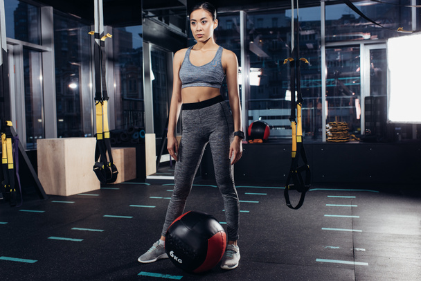 стройная азиатка, стоящая возле медицинского мяча в спортзале
 - Фото, изображение