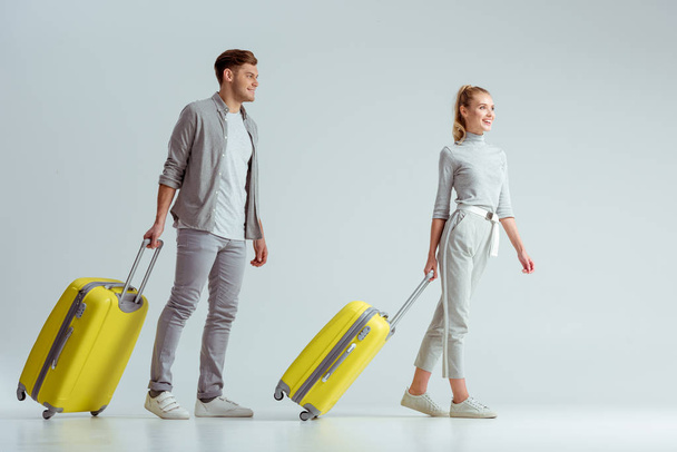 couple souriant portant des valises jaunes sur fond gris, concept de voyage
 - Photo, image