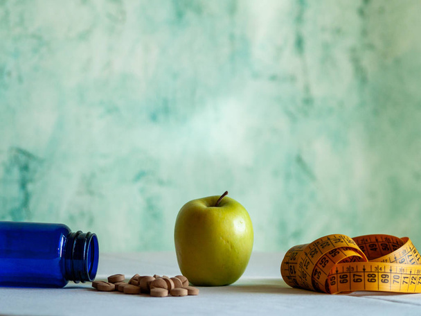 Jabłko, centymetrem i niebieski pojemnik z włókien roślinnych pigułki na stole - Zdjęcie, obraz