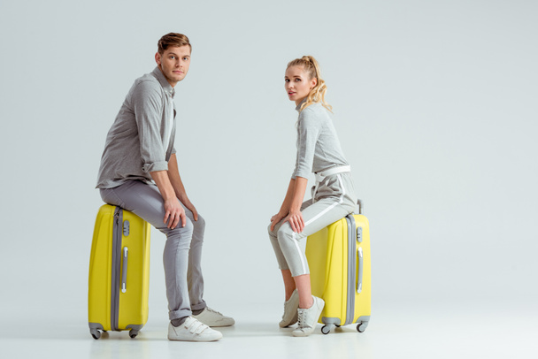 beautiful couple sitting on suitcases and looking at camera on grey background, travel concept - Fotografie, Obrázek
