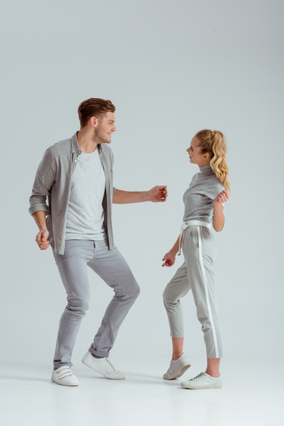 beautiful couple in grey clothing looking at each other and dancing isolated on grey - Фото, изображение