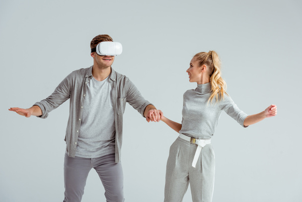 couple in grey clothing holding hands while man experiencing virtual reality isolated on grey - Foto, Imagen