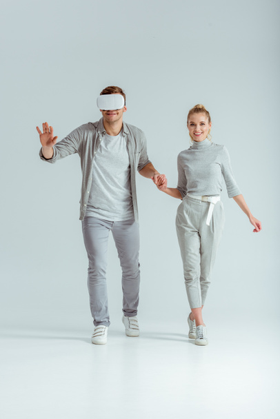 usmívající se pár držel ruku když člověk zažívá virtuální realita na šedém pozadí - Fotografie, Obrázek
