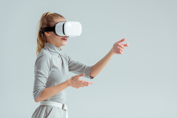 surprised woman gesturing while having virtual reality experience isolated on grey - Foto, Imagen