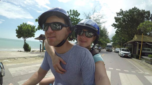 Радостная молодая пара едет на скутере мимо экзотического песчаного берега. Его подруга и бойфренд катаются на мотоцикле и осматривают захватывающую дух прибрежную деревню в Таиланде
. - Фото, изображение
