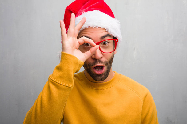Młody człowiek obchodzi Boże Narodzenie trzymając pewnie robi ok gest na oko prezenty - Zdjęcie, obraz