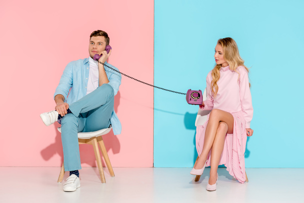 dissatisfied woman holding purple vintage telephone while man talking with pink and blue background - Photo, Image