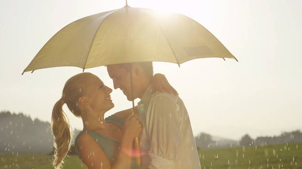 CLOSE UP, LENS FLARE: Happy boyfriend dips his lovely blonde girlfriend while they dance in the idyllic countryside. Cheerful young man and woman in love dance passionately despite the summer rain. - Фото, зображення
