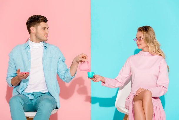pohledný muž, který držel hraček džbán na mléko zatímco žena držící šálek kávy na růžové a modré pozadí - Fotografie, Obrázek