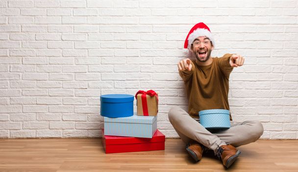 Mladý muž sedí s dárky slavit Vánoce, veselý a usměvavý - Fotografie, Obrázek