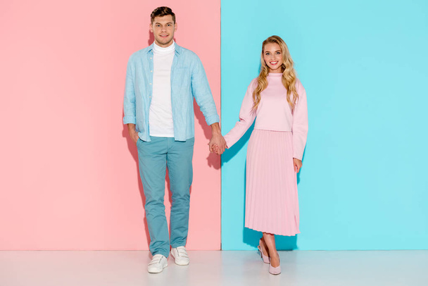 beautiful couple holding hands and looking at camera on pink and blue background - Fotó, kép