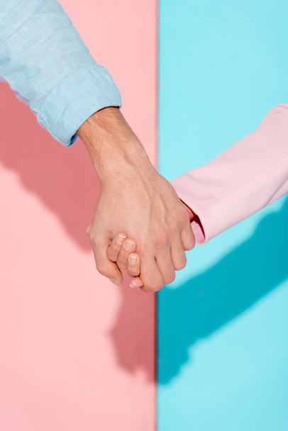 bijgesneden weergave van paar hand in hand op de roze en blauwe achtergrond - Foto, afbeelding