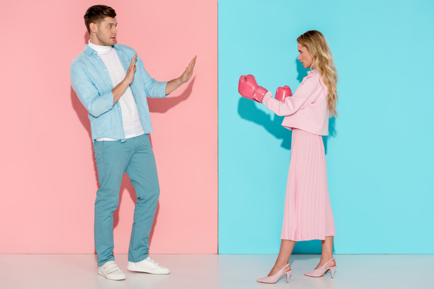 scared man gesturing with hands near aggressive woman in pink boxing gloves on pink and blue background - Photo, Image