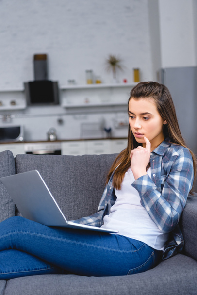 thoughtful young woman sitting on couch and using laptop - Foto, imagen