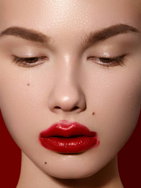 Cosmetics, makeup and trends. Bright lip gloss and lipstick on lips. Closeup of beautiful female mouth with red lip makeup. Beautiful part of female face. Perfect clean skin in red light - Photo, Image