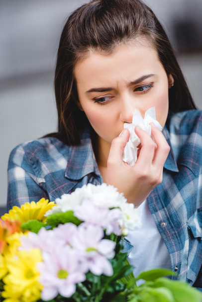 young woman with allergy holding facial tissue and looking at flowers  - Foto, Imagen