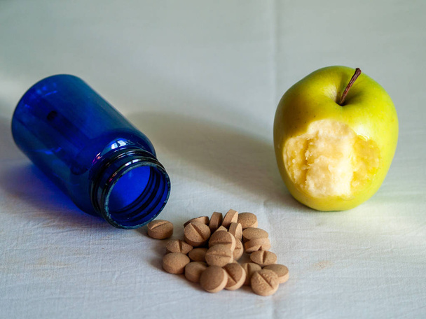 Укушенное яблоко и синий контейнер с таблетками растительного волокна на столе
 - Фото, изображение