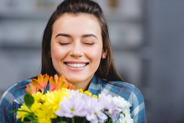 Szczęśliwa młoda kobieta z zamkniętymi oczami, posiadający piękne kwiaty w domu  - Zdjęcie, obraz