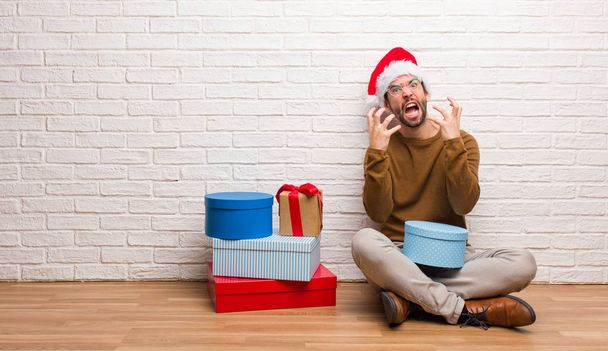 Junger Mann, der mit Geschenken Weihnachten feiert, wütend und aufgebracht - Foto, Bild