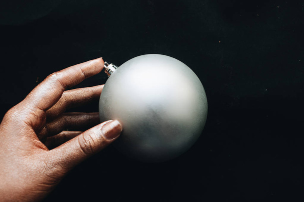 mano femenina sosteniendo gris bola de Navidad sobre fondo negro
  - Foto, imagen