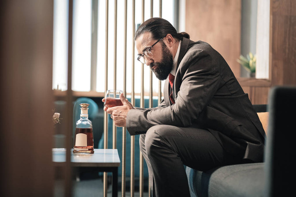 Mature experienced economist sitting in hotel lobby and drinking whisky - Фото, зображення