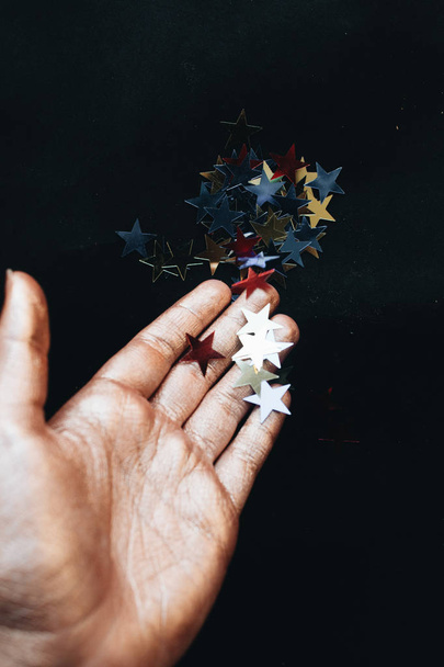 female hand holding stars confetti, black background - Photo, image