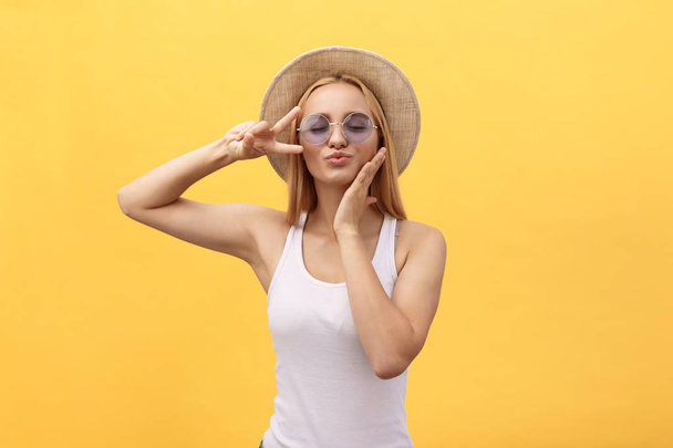 Self portrait of charming cheerful girl shooting selfie on front camera gesturing v-sign peace symbol with fingers isolated on yellow background - Photo, Image