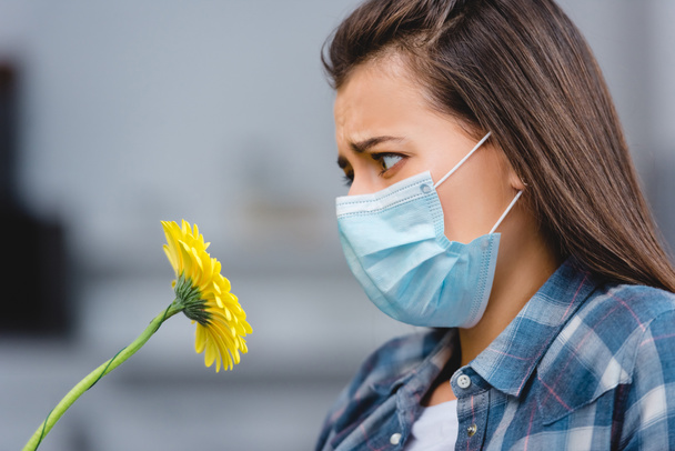 a fiatal nő, allergia, orvosi maszkot visel, és látszó-on virág oldalnézete  - Fotó, kép