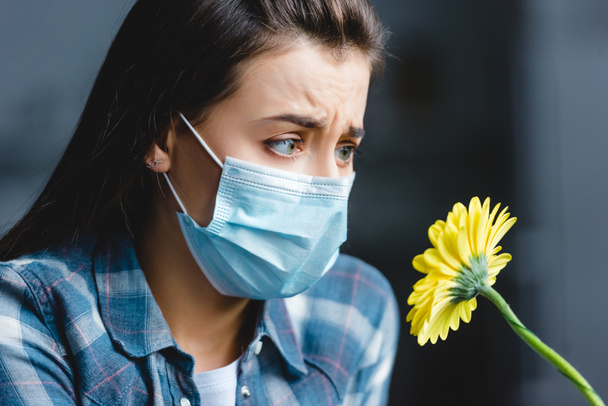 κορίτσι με αλλεργία, φορώντας ιατρική μάσκα και κοιτάζοντας λουλούδι  - Φωτογραφία, εικόνα