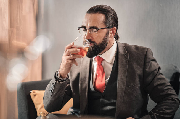Bearded businessman wearing vest and jacket drinking cognac - Foto, Bild