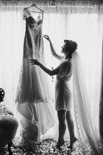 Стильная невеста-брюнетка в шелковом халате и длинном вуалью утром идет к своему изумительному свадебному платью. Чувственный портрет счастливой женщины модели, готовящейся к свадьбе
 - Фото, изображение