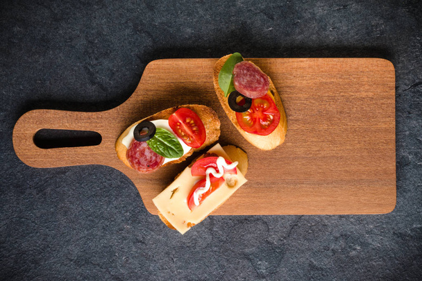 Open faced sandwich canape or crostini on a wooden serving board on dark stone  background closeup. Top view. - Фото, зображення