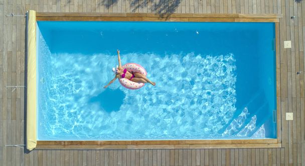Счастливая белая женщина, катающаяся вокруг кристально чистого бассейна на своем прохладном надувном пончике. Радостная женщина-туристка отдыхает на забавной платформе в течение выходного дня в роскошном бассейне
. - Фото, изображение