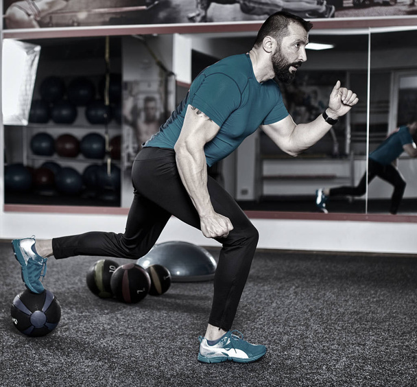 Fitness trainer executing lunges with heavy medicine ball - 写真・画像