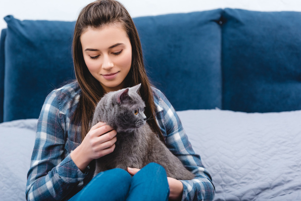 happy young woman stroking cute grey cat in bedroom - Фото, зображення