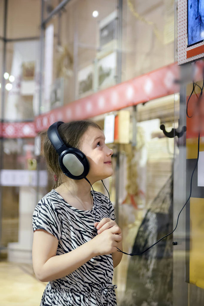   chica en el museo escuchando información interesante sobre la exposición a través de auriculares
.   - Foto, Imagen