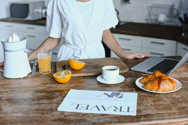 imagen recortada de chica de raza mixta en bata blanca de pie en la mesa por la mañana en la cocina
 - Foto, Imagen