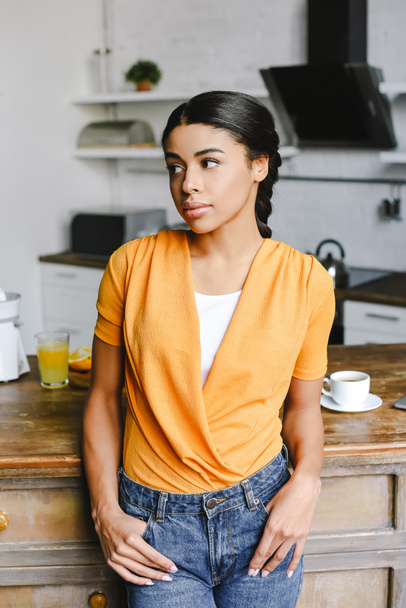 attractive mixed race girl in orange shirt looking away in kitchen - Фото, зображення