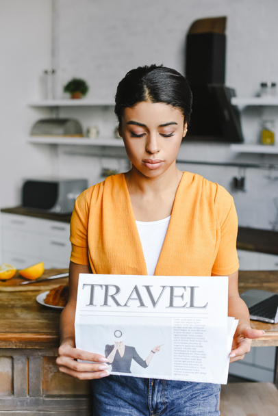 beautiful mixed race girl in orange shirt reading travel newspaper in kitchen - Photo, Image