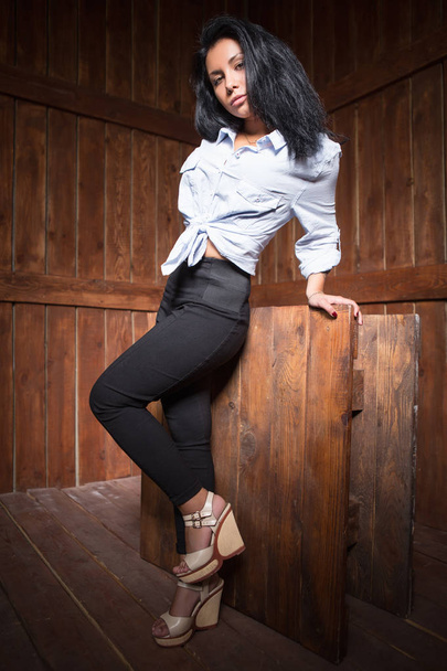 mujer joven en camisa blanca y pantalones negros posando en el interior de madera rústica
 - Foto, Imagen