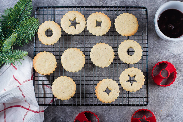 Holiday Sweet Food. Process making of cookies. Christmas Linzer cookies with red berry jam on gray concrete table background. Top view, flat lay - Photo, Image