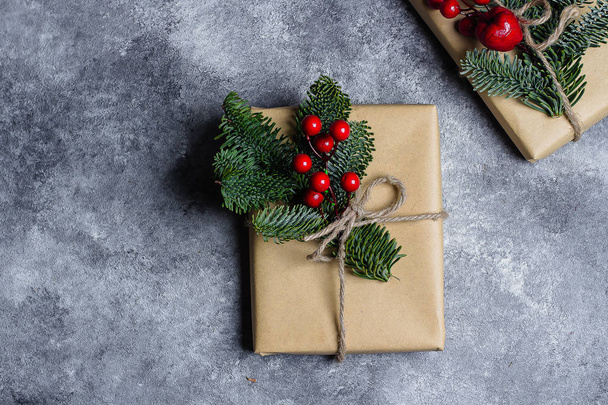 Christmas Gift box verpakt door Kraft papier en ingericht door een tak van de zilverspar en rode bessen op concrete tabelachtergrond. Het concept van Kerstcadeaus en wintervakantie. Flat lag met kopie ruimte. - Foto, afbeelding
