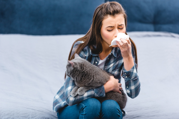 girl with allergy holding facial tissue and british shorthair cat at home  - Fotó, kép