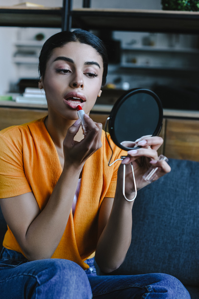 beautiful mixed race girl in orange shirt applying red lipstick at home - Photo, Image