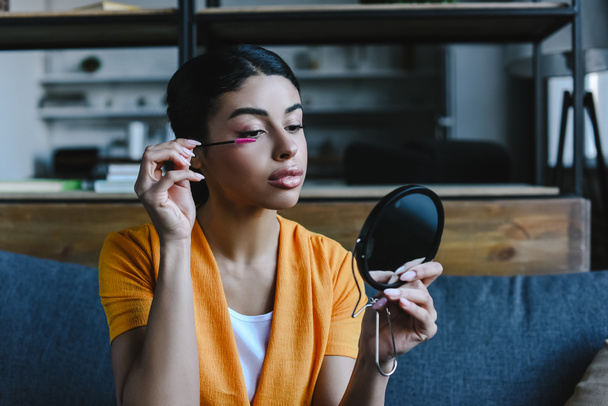 beautiful mixed race girl in orange shirt applying mascara at home - Photo, Image
