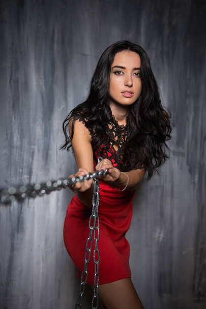 Retrato de mujer joven elegante en rojo vestido corto tirando de cadenas
 - Foto, imagen
