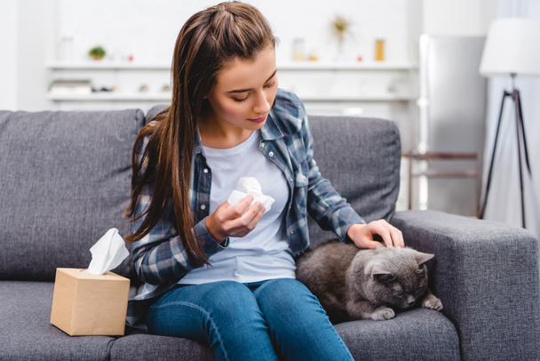 chica con alergia sosteniendo tejido facial y acariciando gato en sofá
 - Foto, imagen